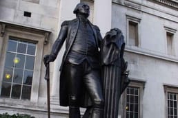 The user asks to translate a title from English to Japanese. The title is a long sentence: "The statue of George Washington in Trafalgar Square in London sits on a base of soil imported from Virginia because Washington swore he would never set foot on British soil again. \"In a square that marks one of Britain's greatest victories stands a reminder of one of its most defeats.\"" Actually the text includes a quote. The user wants only the translated title, nothing else.
We must translate the entire title (the whole text) into Japanese. It's a long title. Provide only the Japanese translation.
Check for any policy issues: It's a historical statement, not disallowed. It's fine.
We must output only the translation, no extra